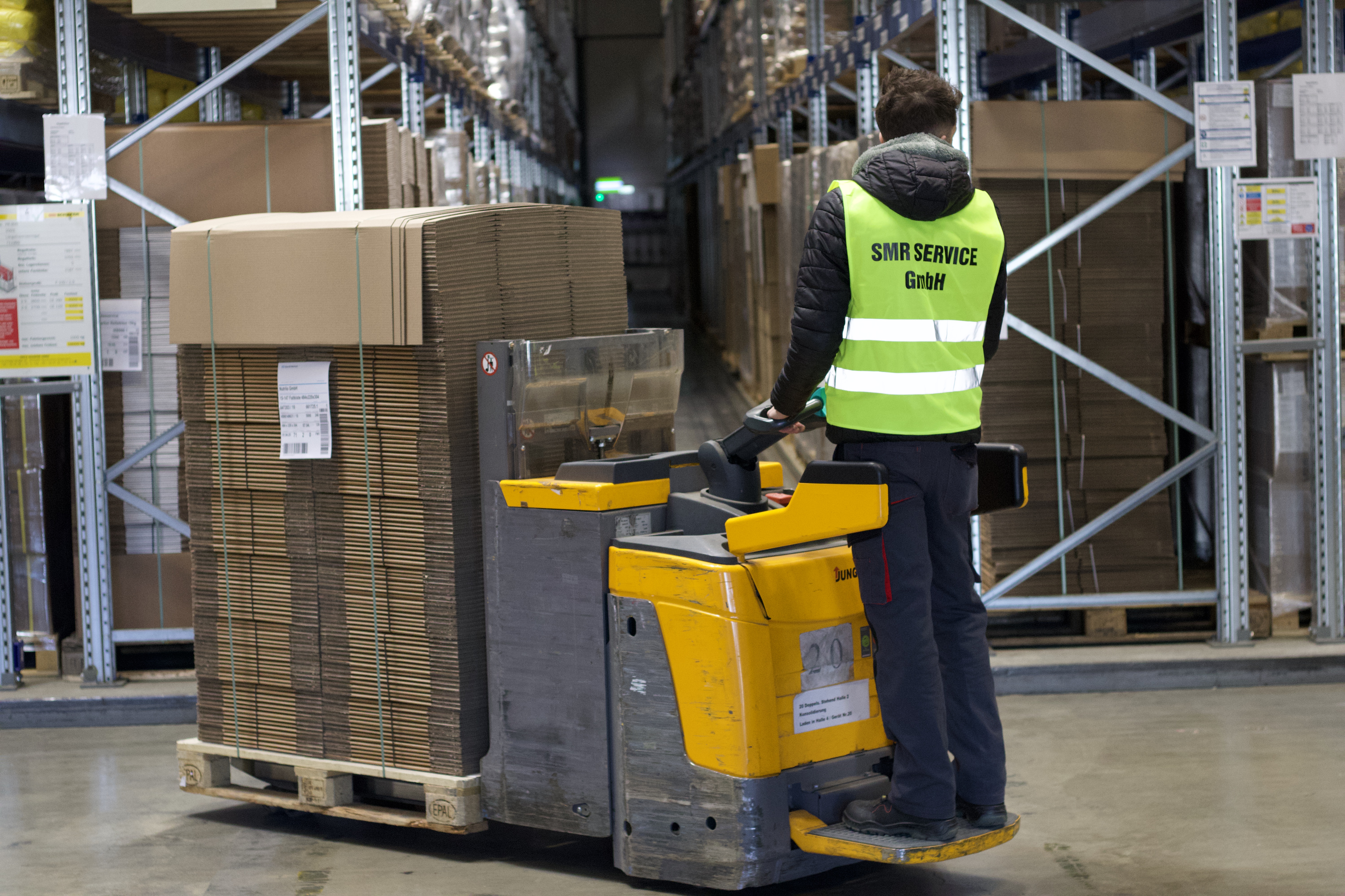 Mitarbeiter transportiert Kartonagen im Lager mit Niederhubwagen von Jungheinrich