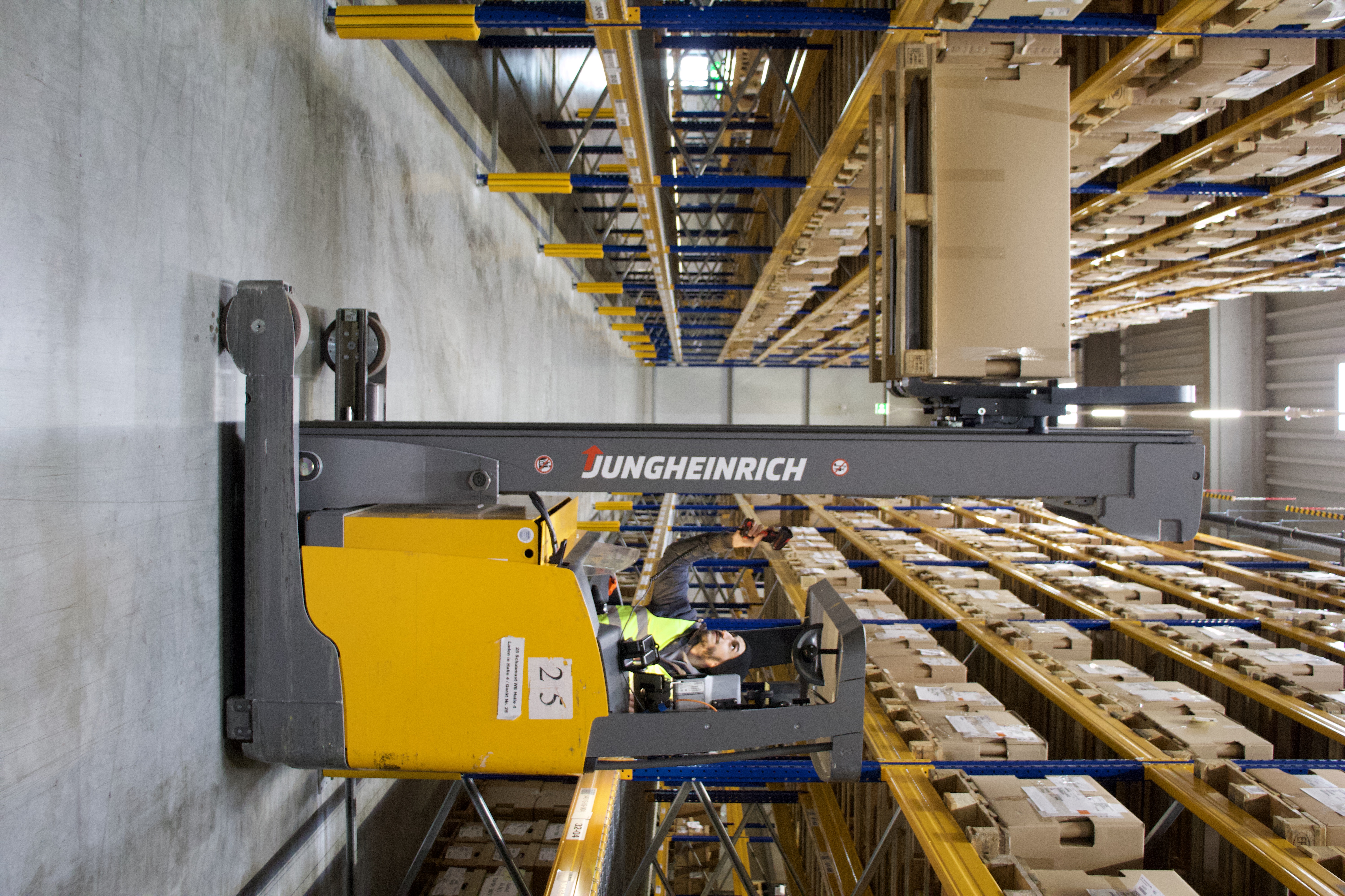 Logistikmitarbeiter scannt Palette beim Einlagern mit Hochregalstapler im Lager